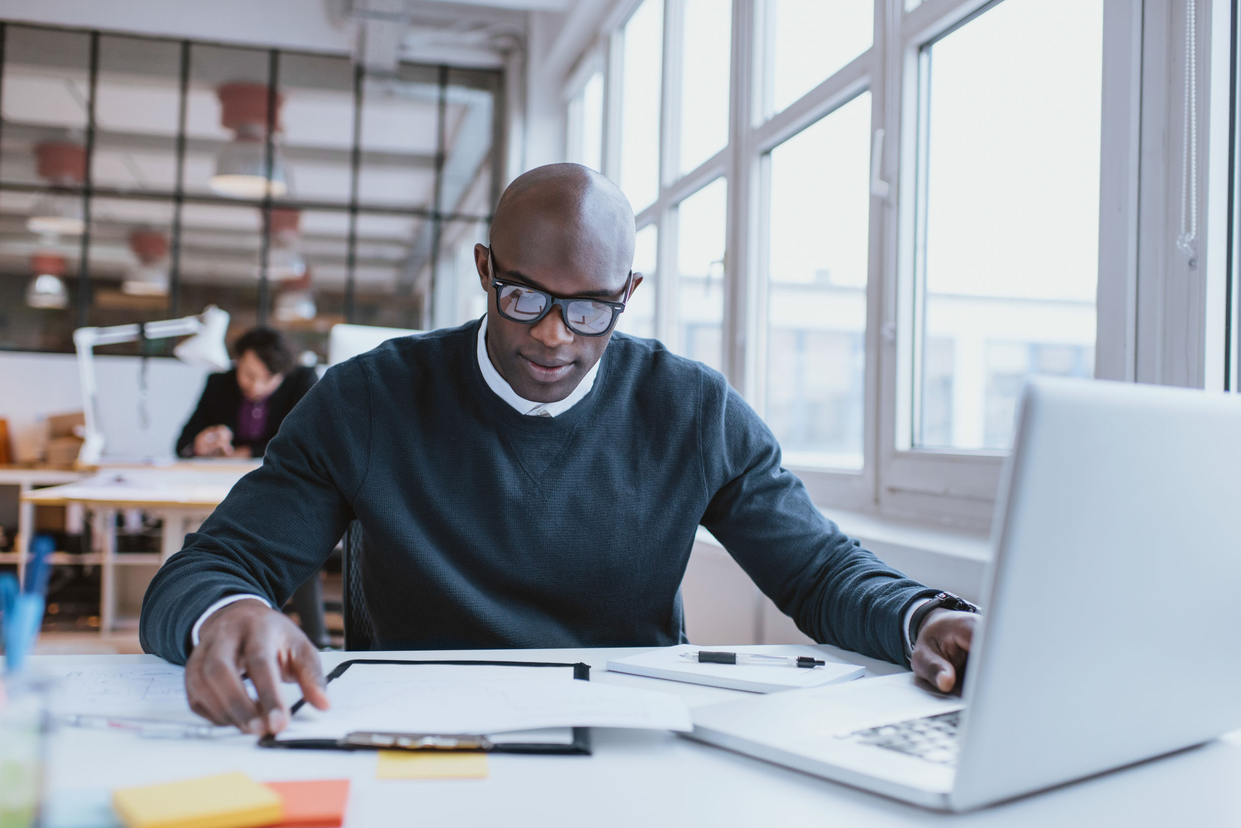 young african executive sitting at his desk with laptop reading a document. african man working in office.