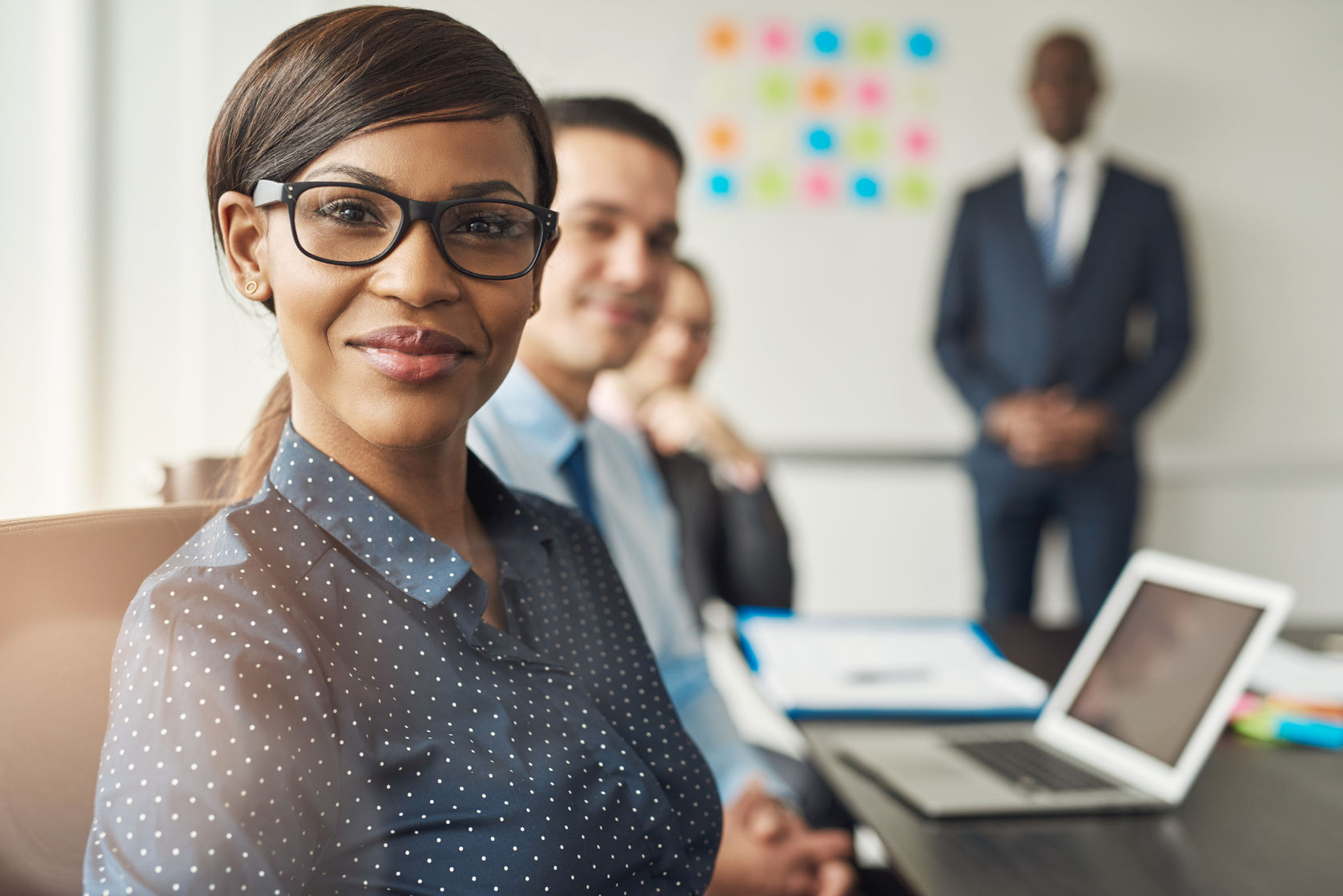 beautiful cheerful professional woman wearing eyeglasses seated with male co-workers and team leader in conference room at work