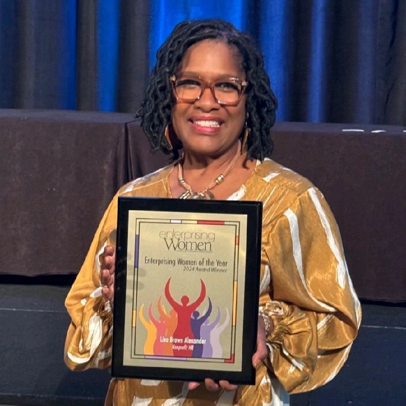 Lisa Brown Alexander smiling holding a plaque for the 2024 Enterprising Women of the Year Award.